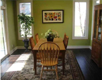 A dining room with olive green walls, a light wood table and a floral area rug.