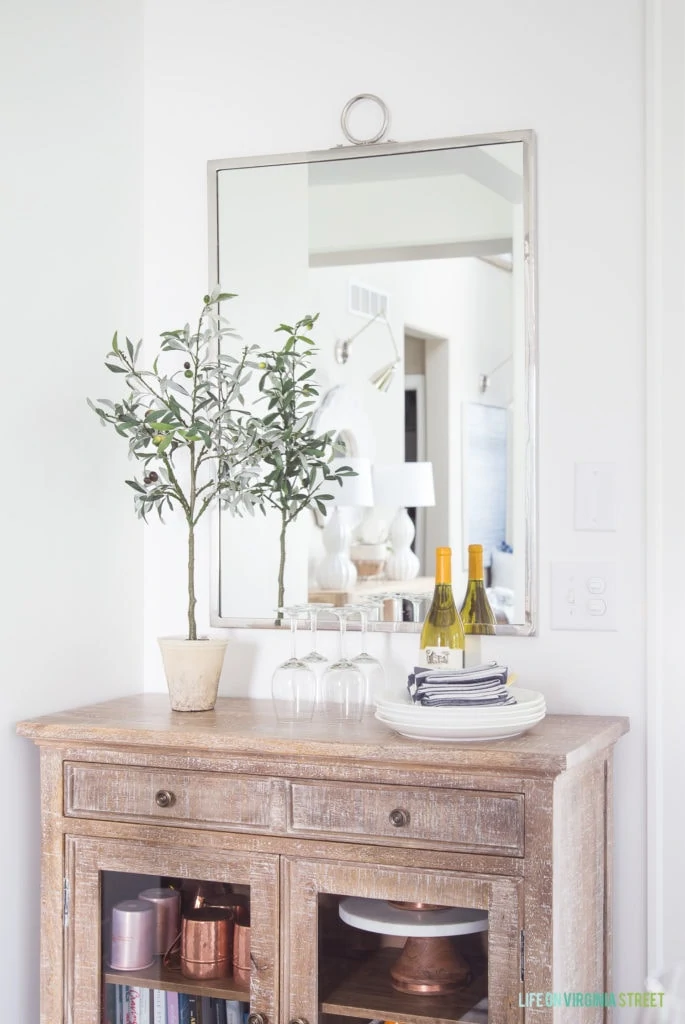 A small wood buffet table with a silver mirror, faux olive leaf topiary, copper accents and blue and white striped napkins.