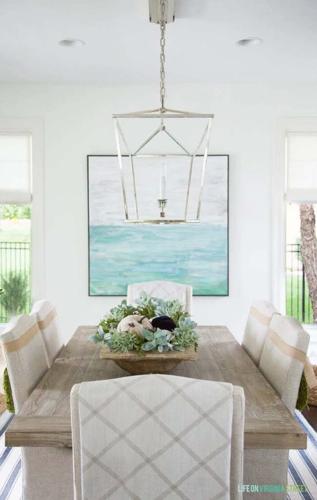 Dining table decorated for fall with chandelier over top and a ocean blue picture behind it.