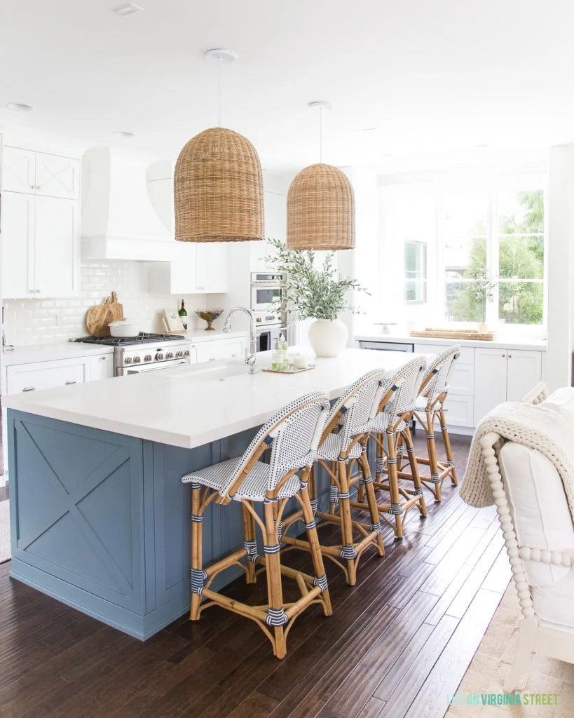 White kitchen with blue island, rattan chairs and light fixtures above the island.