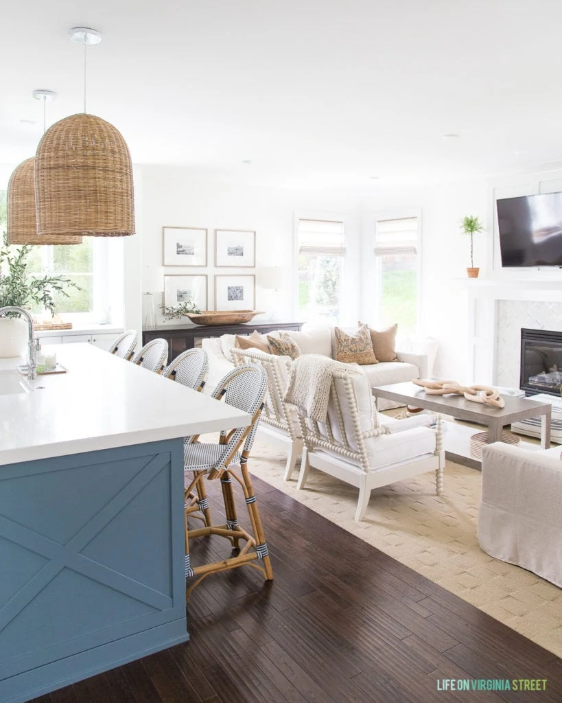 A white TV room off the kitchen with white chairs and couch, plus a fireplace with a TV above it.