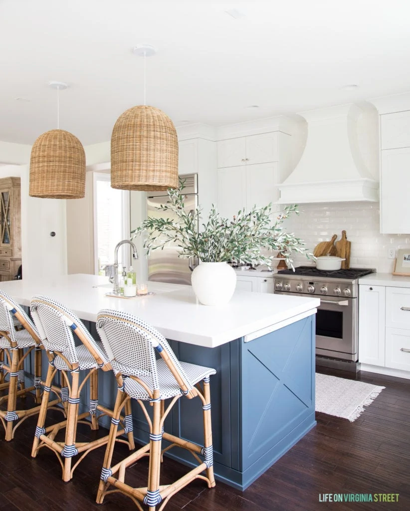A white coastal kitchen with a blue island and wood flooring.