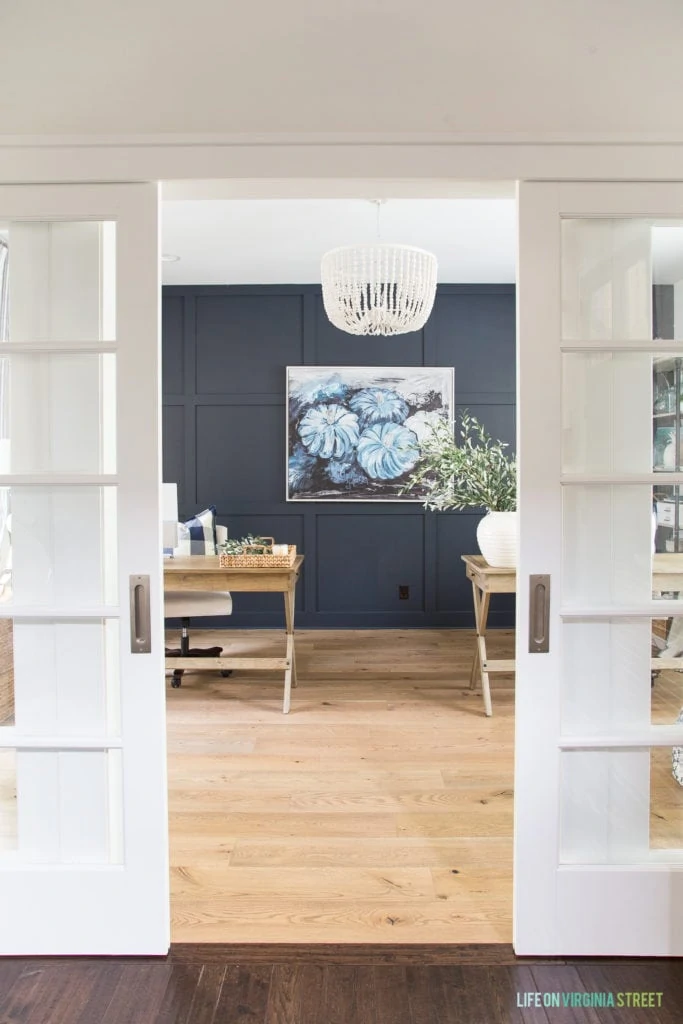 White sliding office doors open into an office with Benjamin Moore Hale Navy walls and white oak hardwood floors.