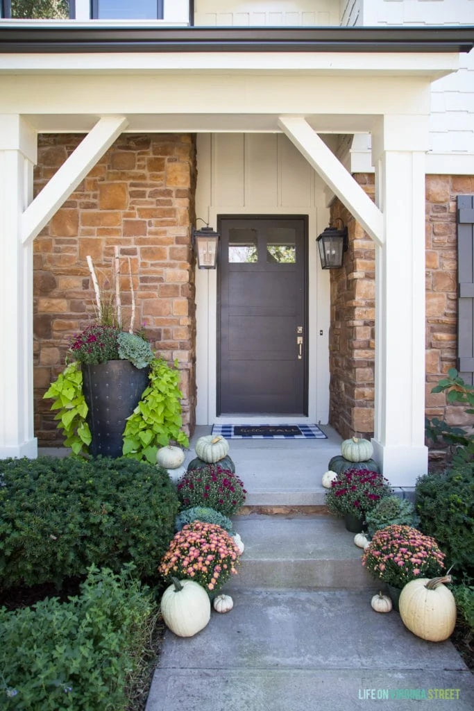 Front porch with white pumpkins, pink and purple flowers in planters beside the walkway.