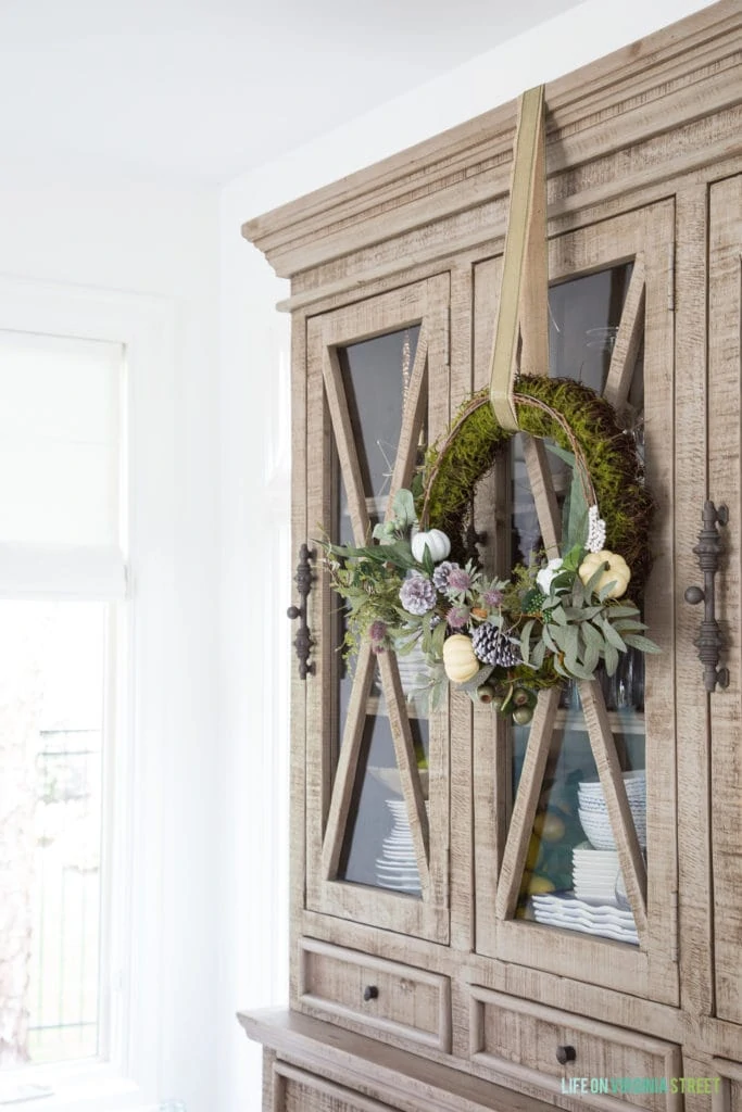 Wooden hutch with a green wreath and flowers on it in fall dining room.