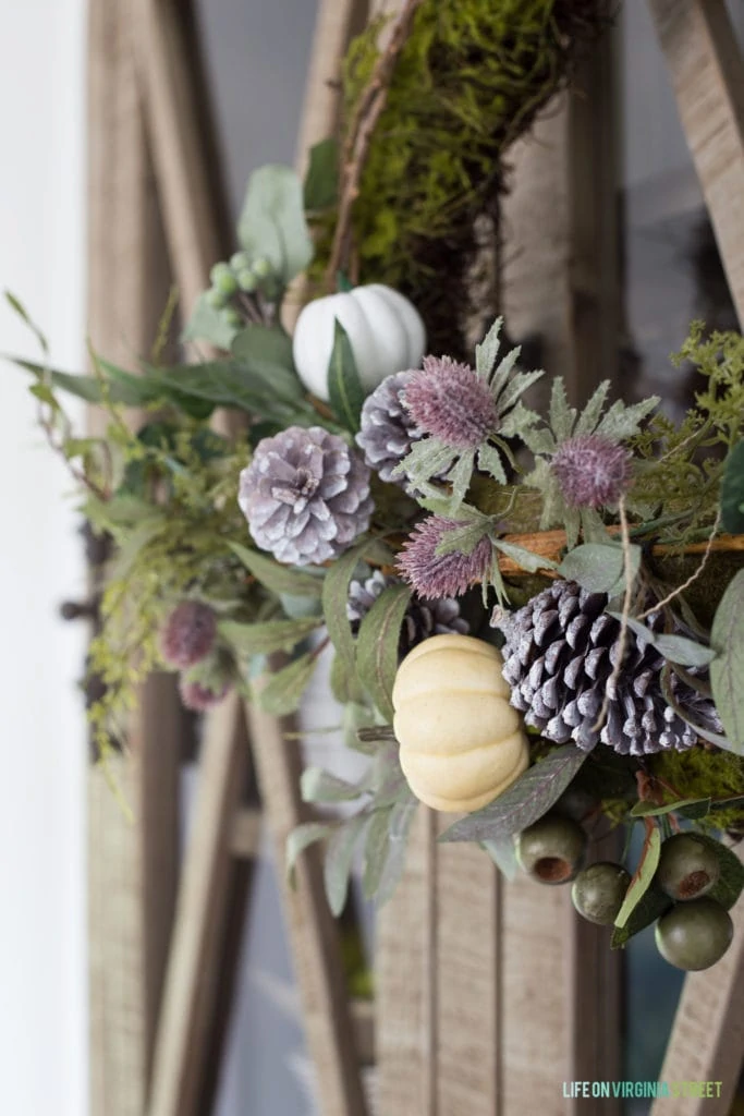 Up close picture of the wreath with the purple pinecones and small pumpkins on it.