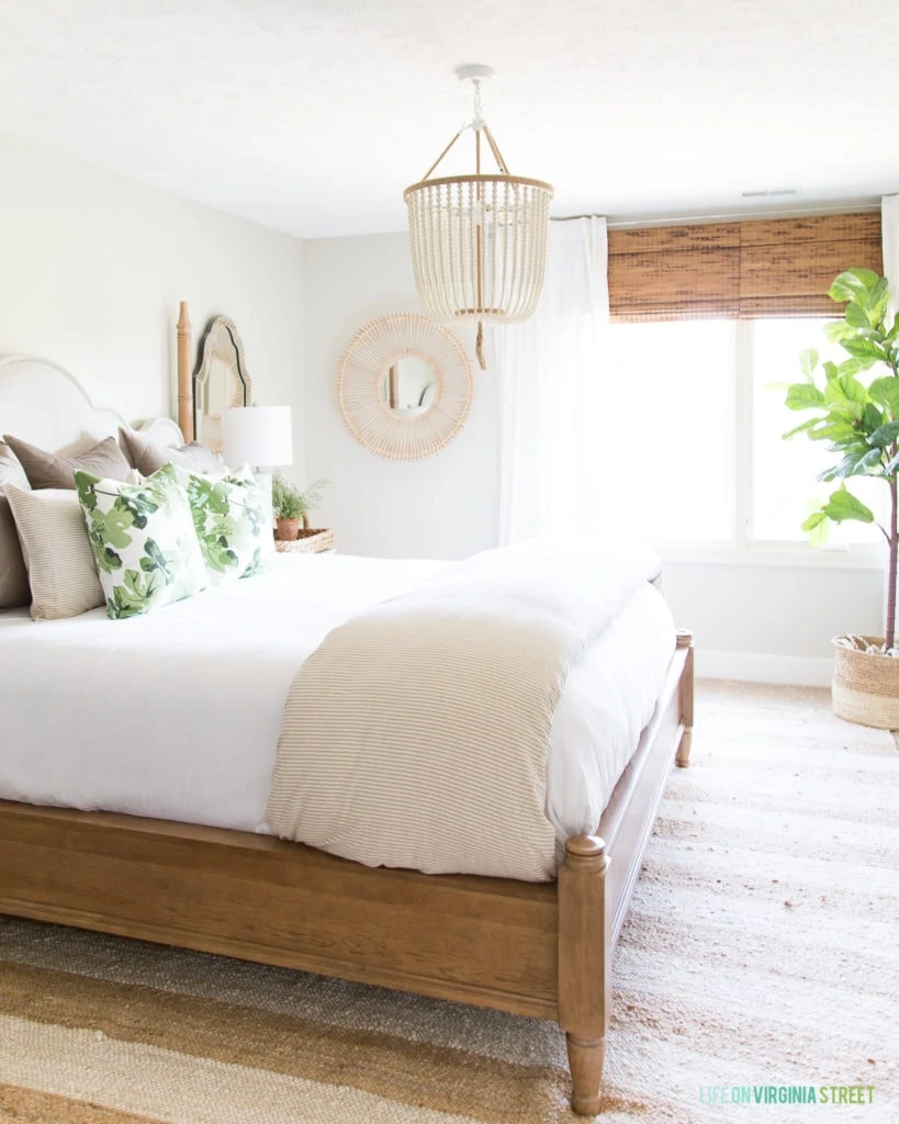 A wooden bed frame with neutral bedding and green and white pillows on the bed.