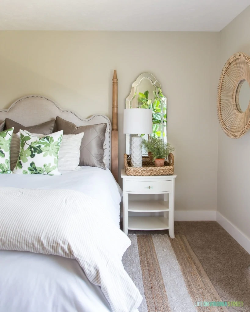 A round rattan mirror is on the side wall beside the bed.