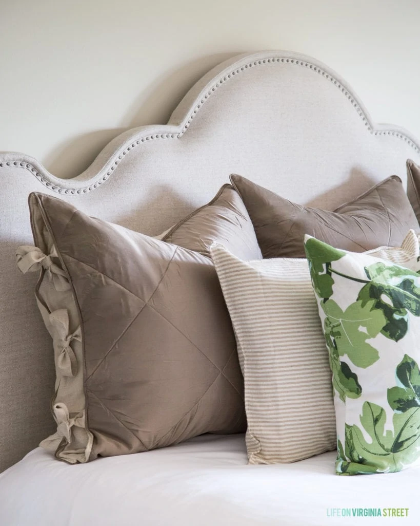 Fig leaf pillows are on the bed with neutral grey pillows.