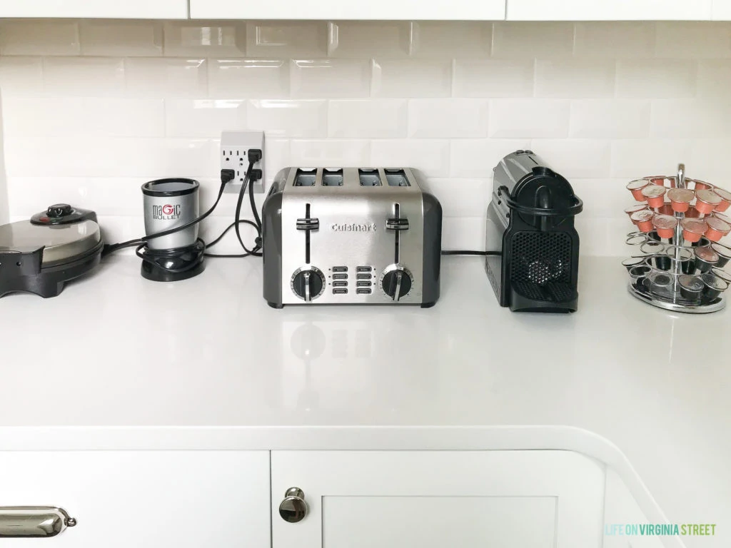 Appliances on the counter such as a toaster, coffee maker and grinder and a waffle maker.