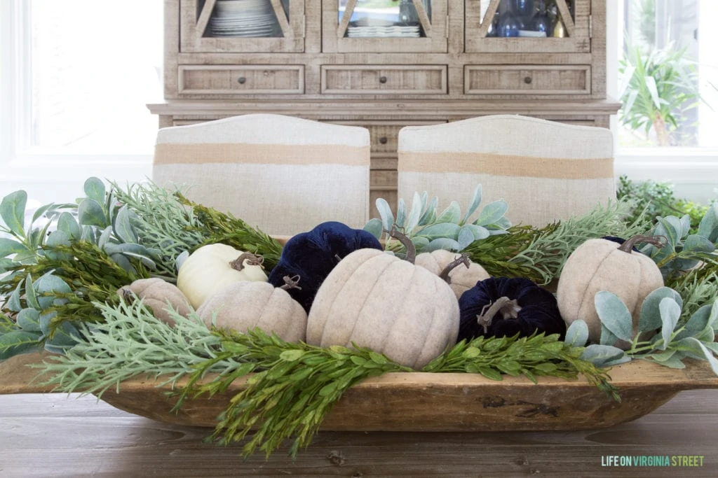 White and dark blue pumpkins sitting in a wooden tray on the table.