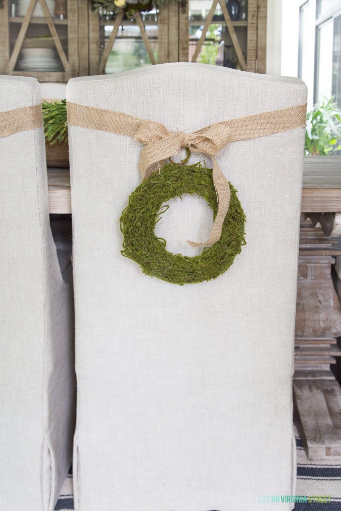 Burlap bow and green wreath on a white chair in the dining room.