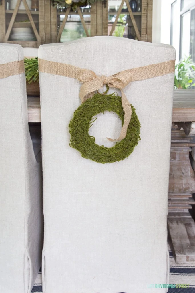 Burlap bow and green wreath on a white chair in the dining room.