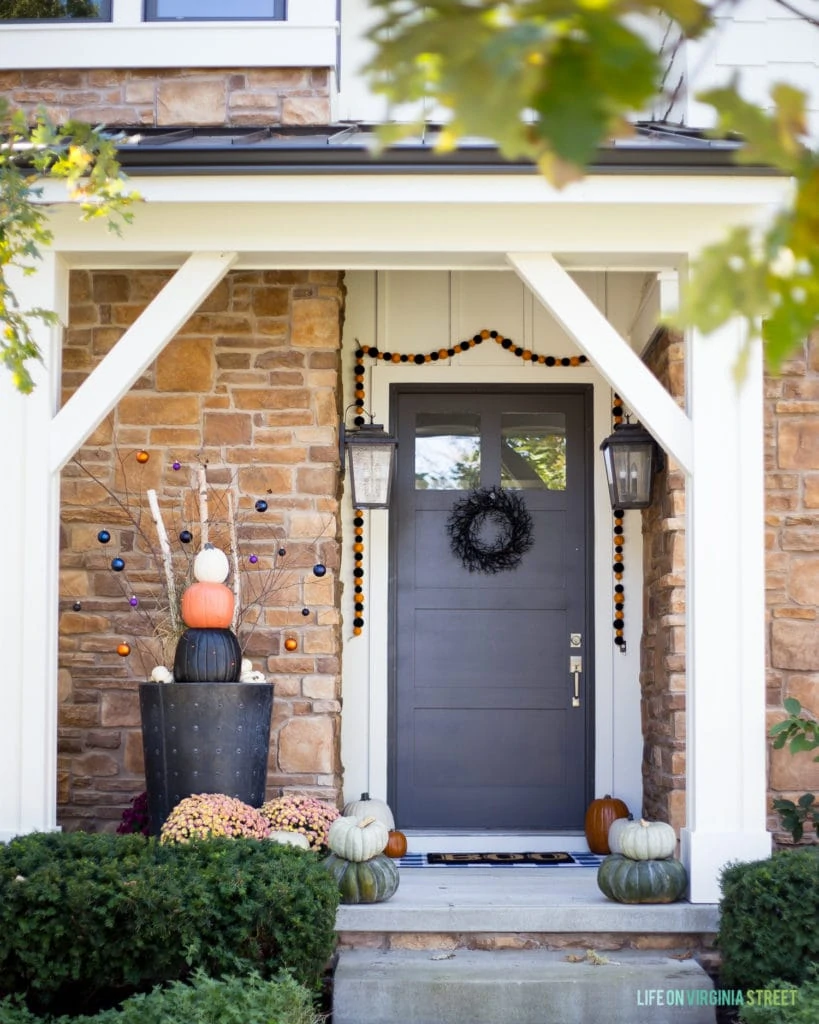 House with a stone front and grey blue door with pumpkins and a black wreath.