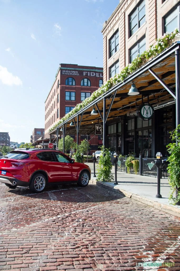 A cobblestone street, and the front of a restaurant with green ivy growing on the posts in front and also on the awning.