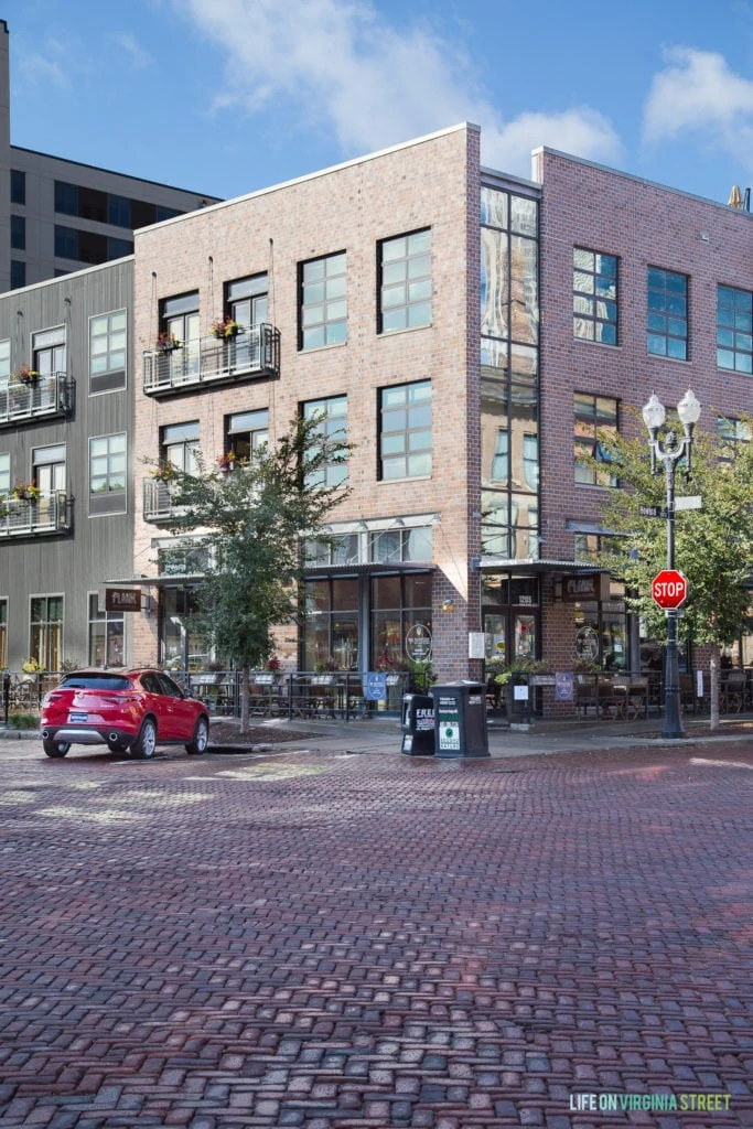 A red car parked outside of a restaurant that has large windows and a brick front.