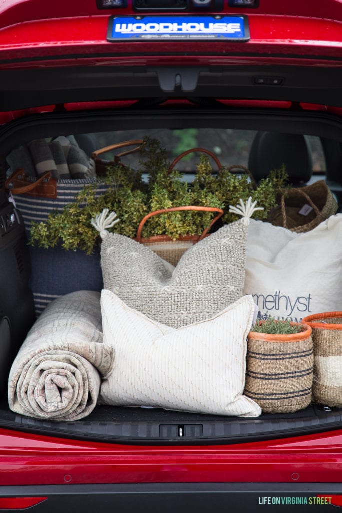 The back of a red car filled with pillows, blanket and plants.