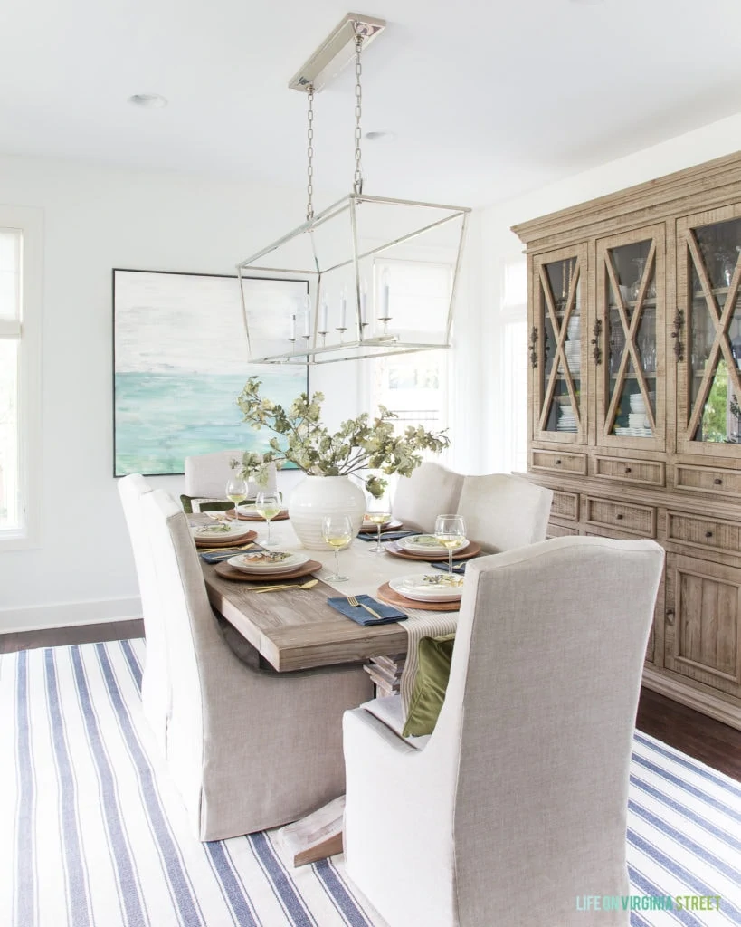 A beautiful fall tablescape with wood chargers, faux oak leaf centerpiece, watercolor pumpkin plates, all in a beautiful coastal dining room.