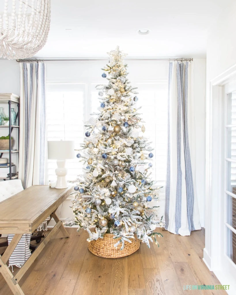 Blue, white and gold flocked Christmas tree on wooden floor in front of window.