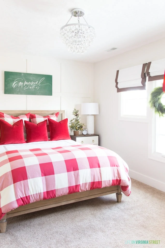 Festive guest bedroom with red and white buffalo check duvet cover, lit faux pine tree, crystal chandelier, and Emmanuel chalkboard canvas art.