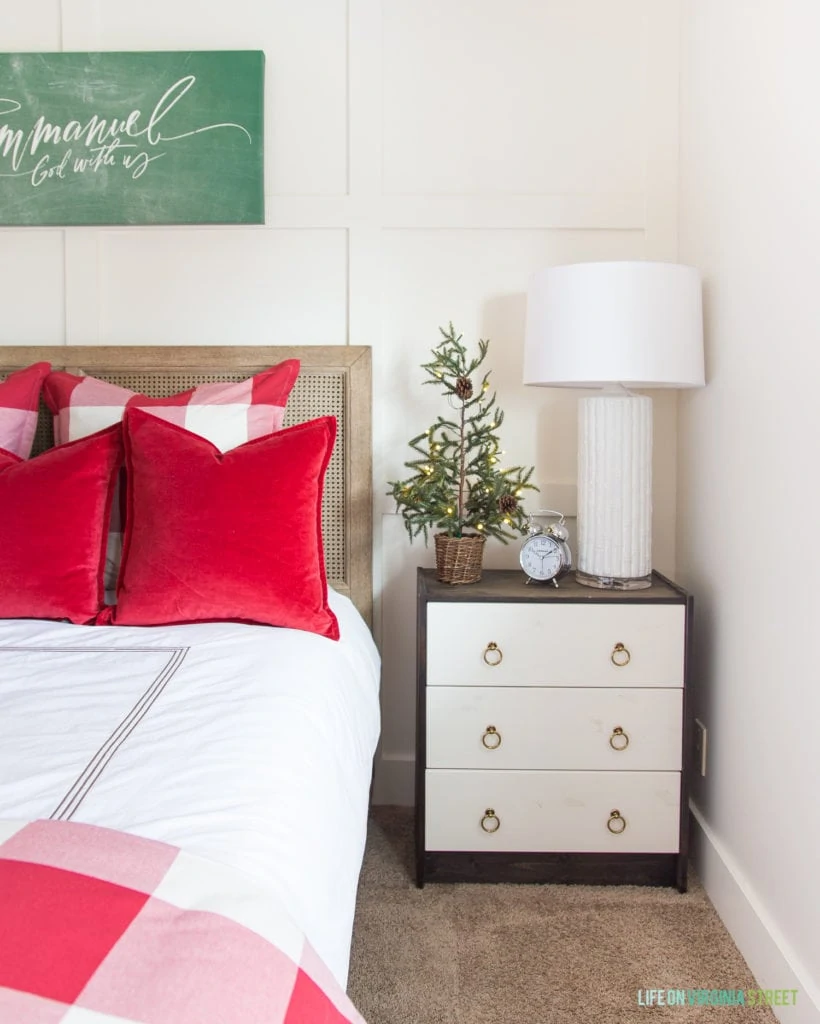 Red and white checkered duvet, red pillows, and a small Christmas tree beside the bed on the side table.