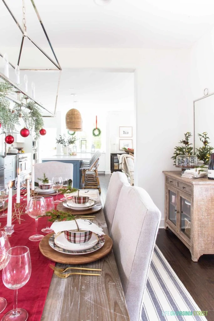 A red plaid Christmas dining room with linen chairs and reclaimed wood dining table. I love the wood chargers, plaid dishes, and gold flatware!