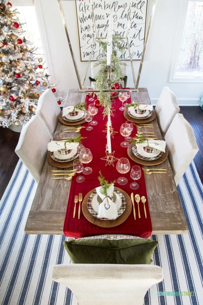 Aerial view of the wooden table with red velvet runner, gold cutlery and Christmas tree in the corner of the room.
