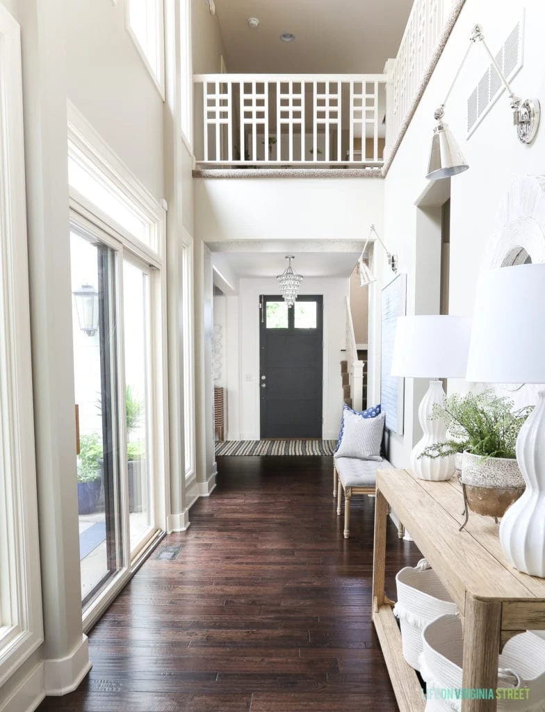 Entryway hallway with grid railings, dark hardwood floors, reclaimed wood console table, chrome swing arm sconces and blue and white accessories.