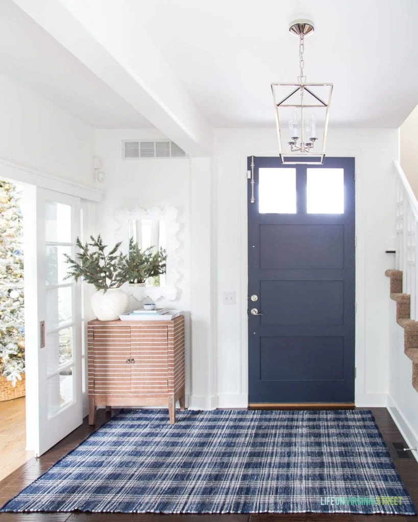 Modern coastal entryway with a Darlana lantern pendant light, navy blue plaid rug, striped wood cabinet and front interior door painted Benjamin Moore Hale Navy.