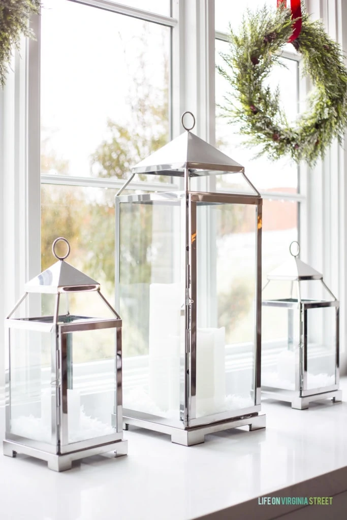 Silver lanterns filled with flickering candles and faux snow. Green wreaths are hung from the windows with red velvet ribbon.