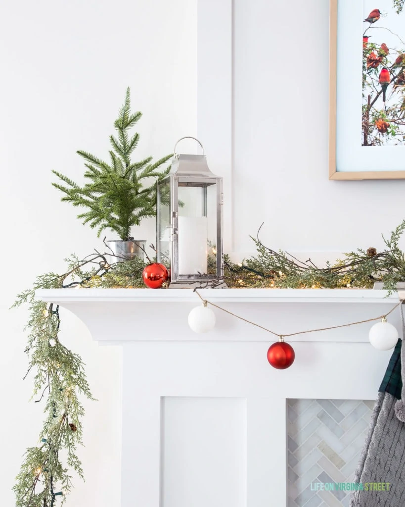A silver lantern with a flameless flickering candle on a simple Christmas mantel.