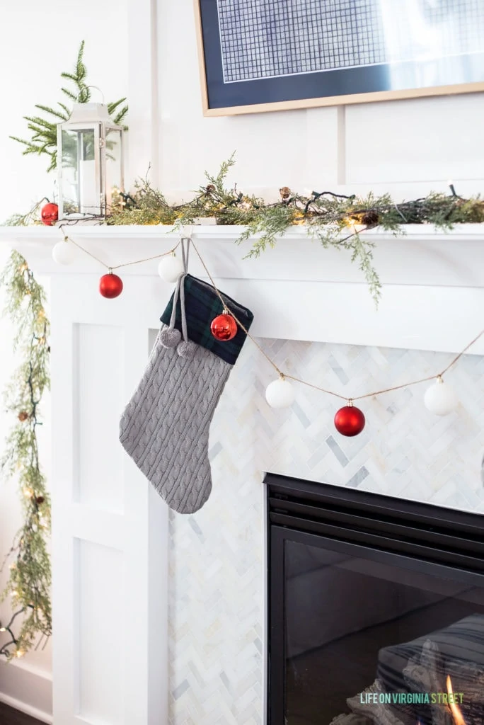 A gray cableknit and plaid stocking on a white mantel with marble herringbone tile.