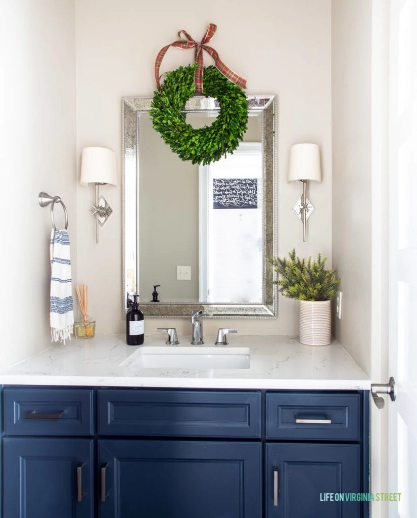 A powder bath room decorated for Christmas! I love the addition of the boxwood wreath hung with a plaid ribbon. The star sconces and navy blue cabinets make this room feel even more festive!