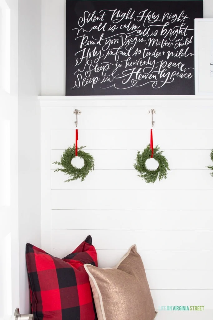 Cute Christmas decorations with buffalo check plaid pillow, a black Silent Night canvas artwork and mini green wreaths hung with red velvet ribbon.