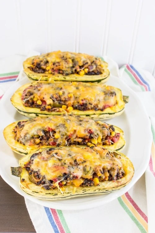 Delicata Squash Stuffed With Tex-Mex Veggie Quinoa four in a row on a white baking dish.