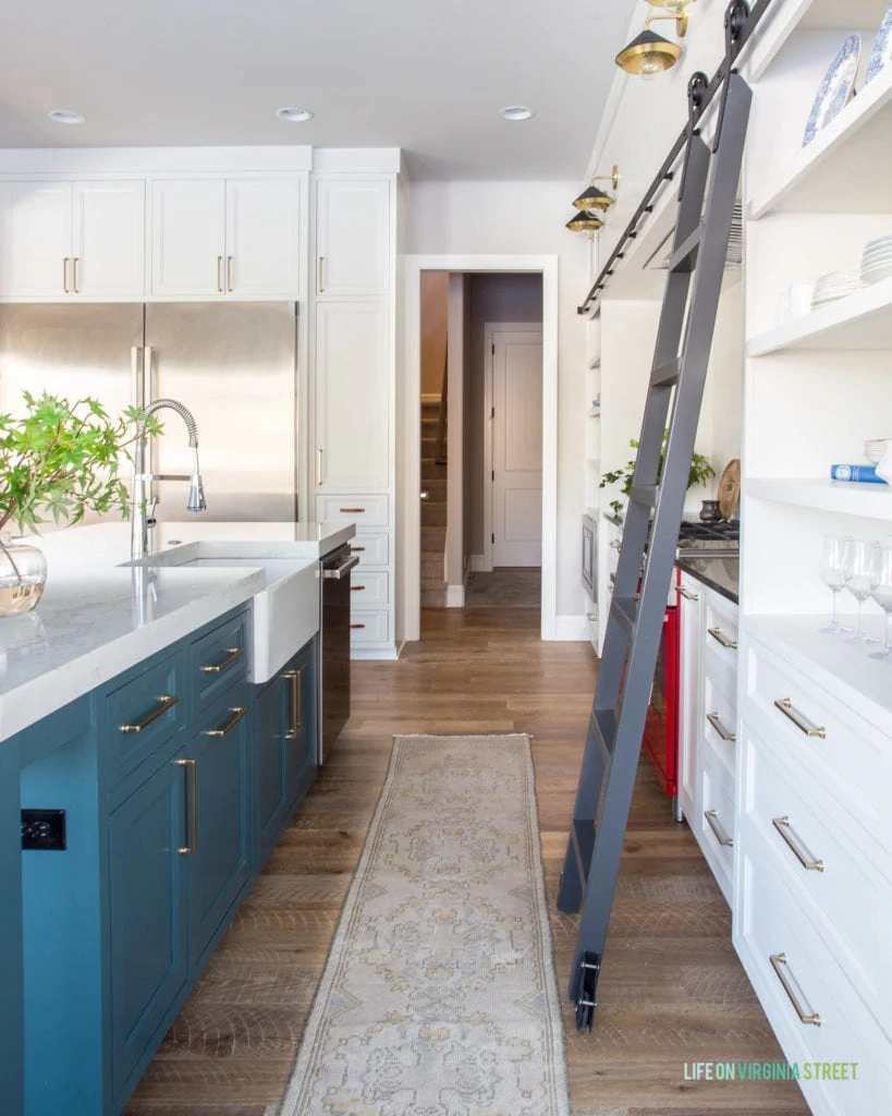 A gorgeous English farmhouse kitchen feature a blue green island (Benjamin Moore Yorkshire Greene), a vintage runner, white cabinets (Benjamin Moore Cloud Cover), and a metal library ladder!