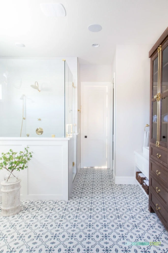 A beautiful English farmhouse bathroom with patterned tile floors, white board and batten, Benjamin Moore Collingwood walls, walnut stained bathroom cabinets, and gold fixtures.