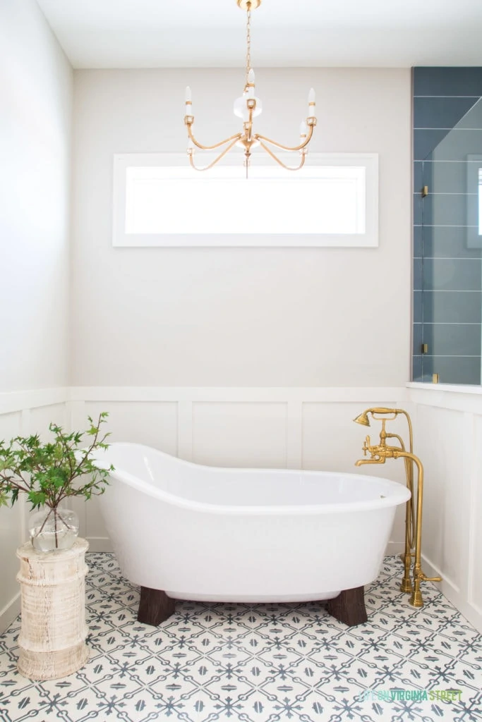 Beautiful pedestal bathtub in a English farmhouse style bathroom. The gray and white patterned floors pair beautifully with the white board and batten and gold fixtures. The walls are Benjamin Moore Collingwood.