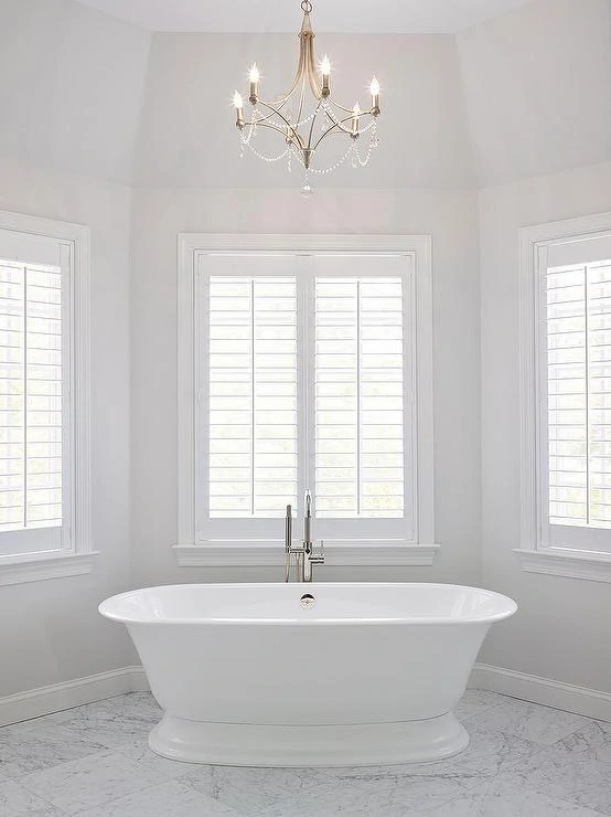 Walls painted Benjamin Moore Paper White in a serene bathroom with a chandelier and plantation shutters.