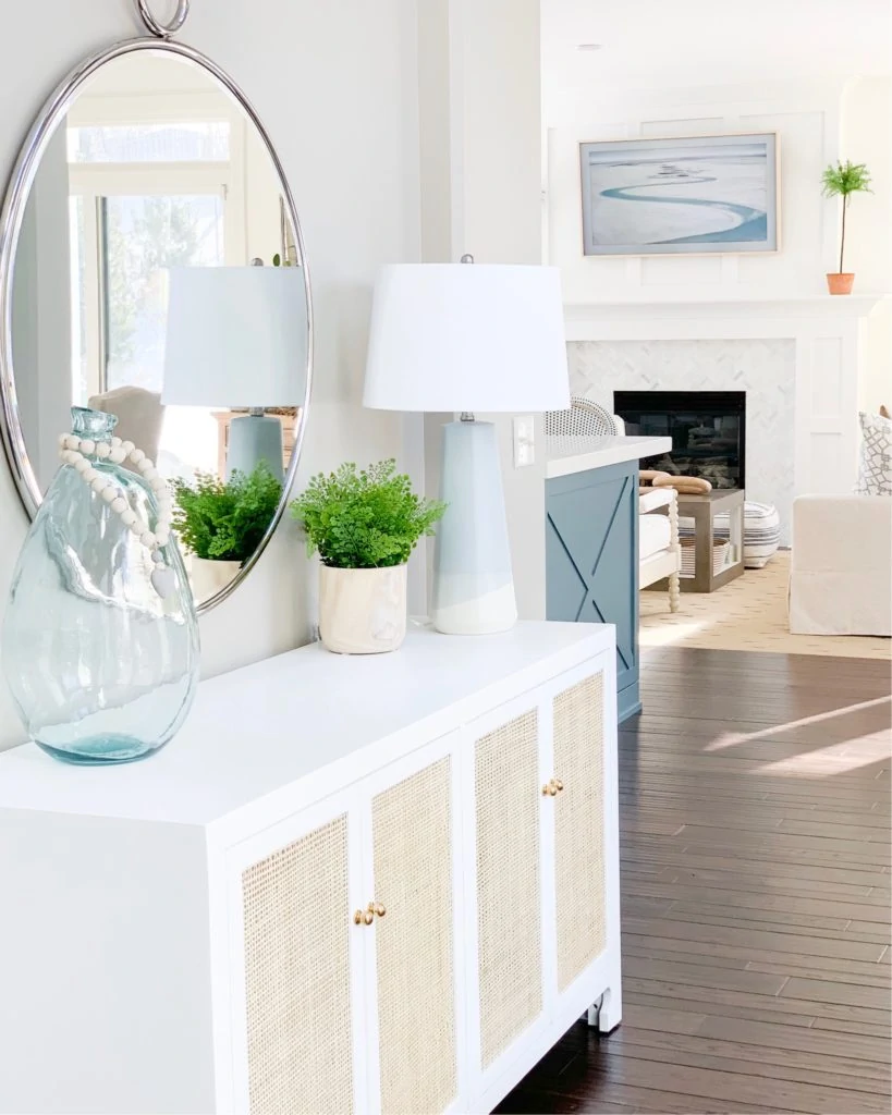 A beautiful dipped ceramic table lamp on a white and cane console table in a coastal inspired entryway. This post has a great variety of stylish table lamps and bedside lamps that work well for all budgets!