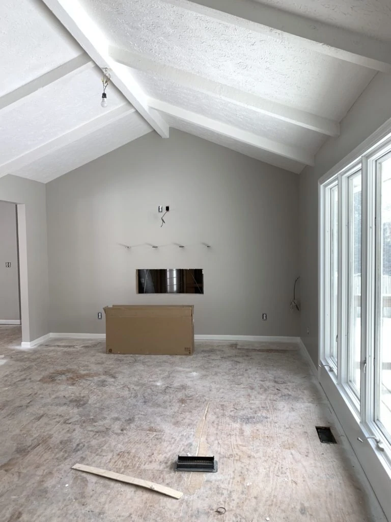 A renovated living room with a white ceiling with beams and walls painted Sherwin Williams Agreeable Gray.