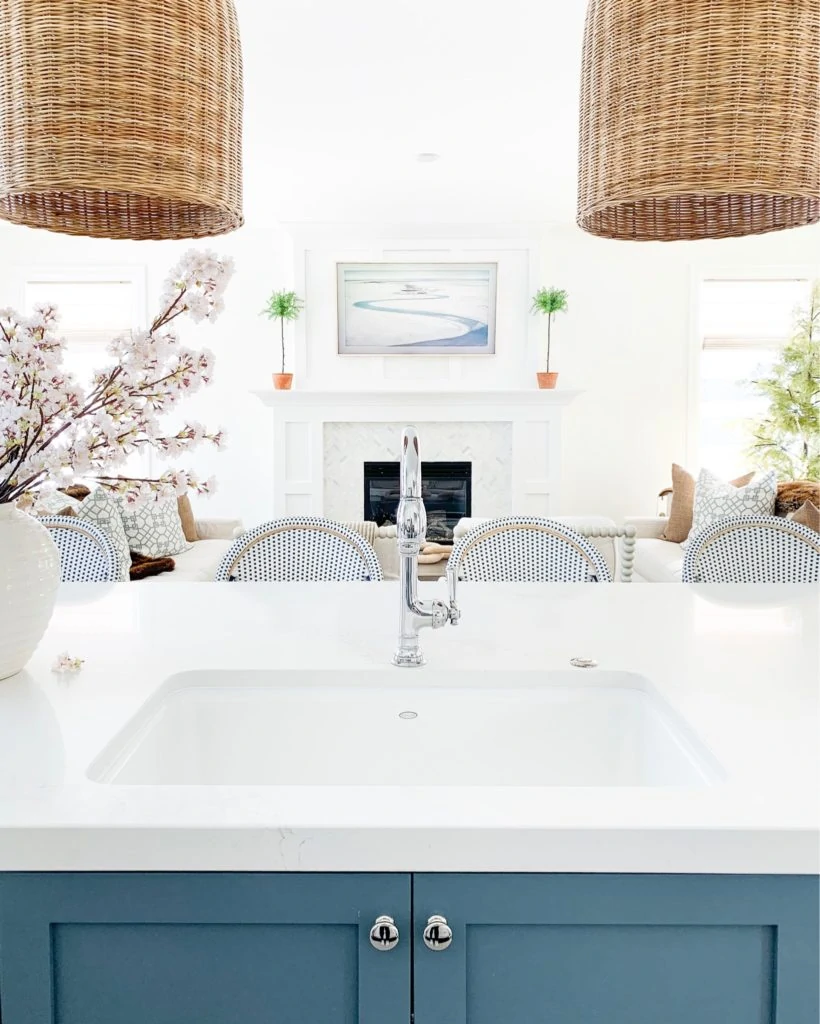 A kitchen sink view with a blue island and basket pendant lights. All made fresh with faux cherry blossom stems for spring!