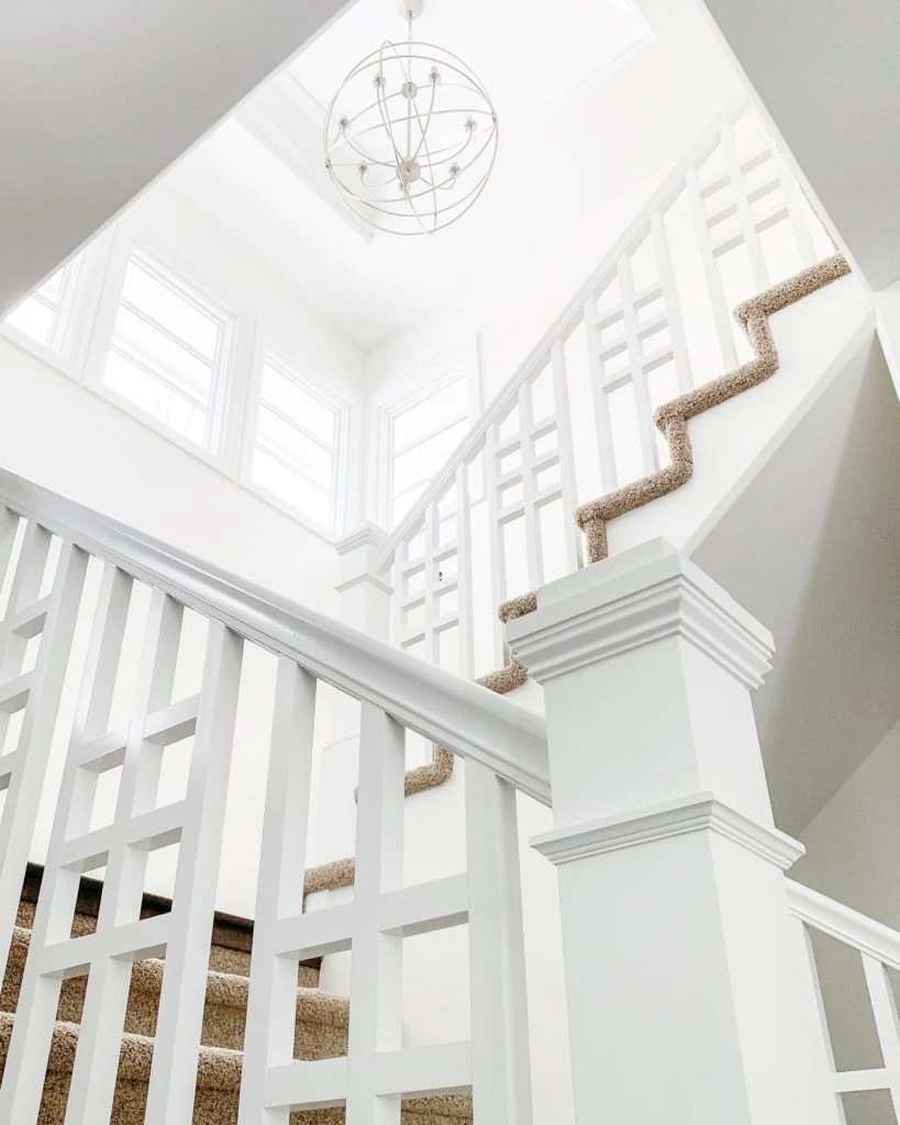 Entryway staircase painted in Benjamin Moore Simply White. Walls are an eggshell finish and the trim is semi-gloss. I love the orb chandelier and the interesting pattern on the staircase railings!