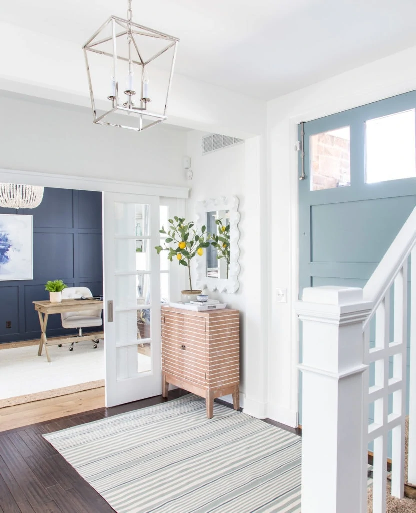 A coastal inspired entryway with a blue gray painted interior front door, a striped rug, white walls and a navy blue wall in the background.