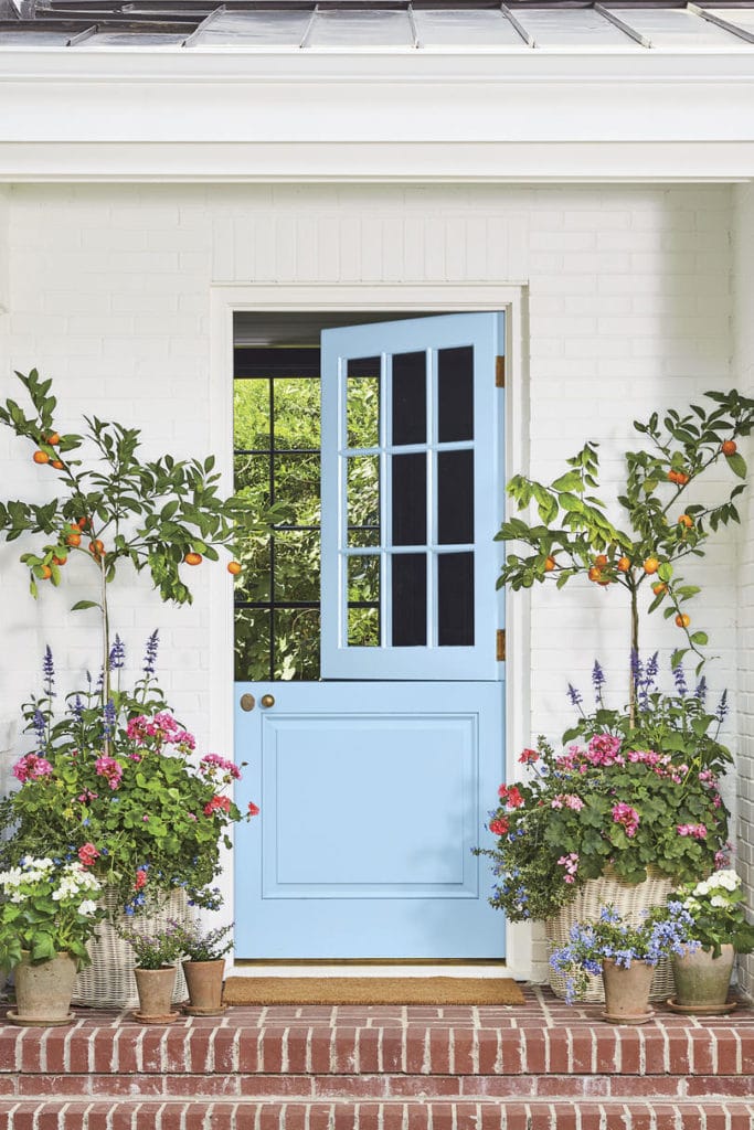 Blue front door, white brick house, with red brick porch steps. Wicker and Terra Cotta Planters with Citrus Trees and Flowers via Southern Living