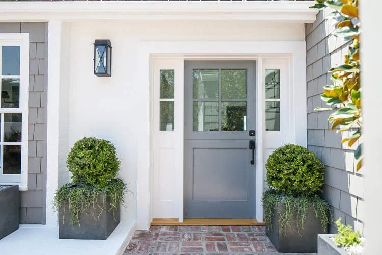 A gray modern coastal home with simple planters filled with boxwoods flanking the front door.