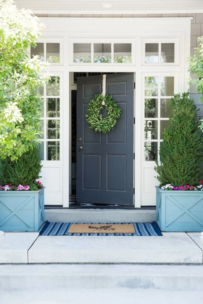 A traditional front porch with blue wood planters filled with boxwood topiaries and impatiens.