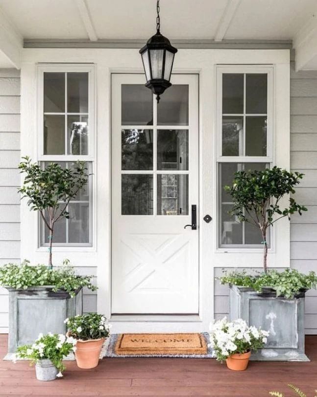 A beautiful gray home with white front door. The galvanized planters are filled with topiaries and the terra cotta pots are filled with white petunias.