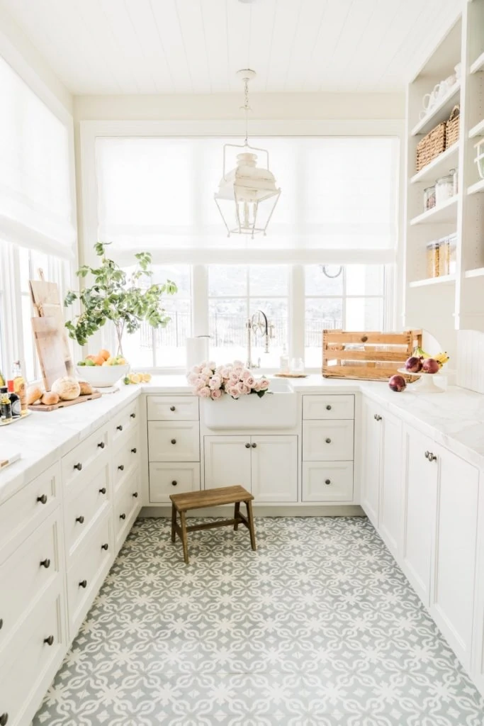 A gorgeous pantry with white cabinets, windows, gray and white patterned cement tile floors, a white lantern and French style accents.