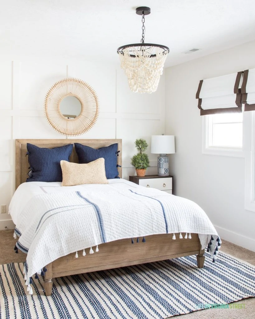 A navy blue and white spring guest bedroom. I love the white wood bead chandelier, the striped rug, the pick-stitch bedding, the rattan mirror and all the other pretty blue and white decor accents!